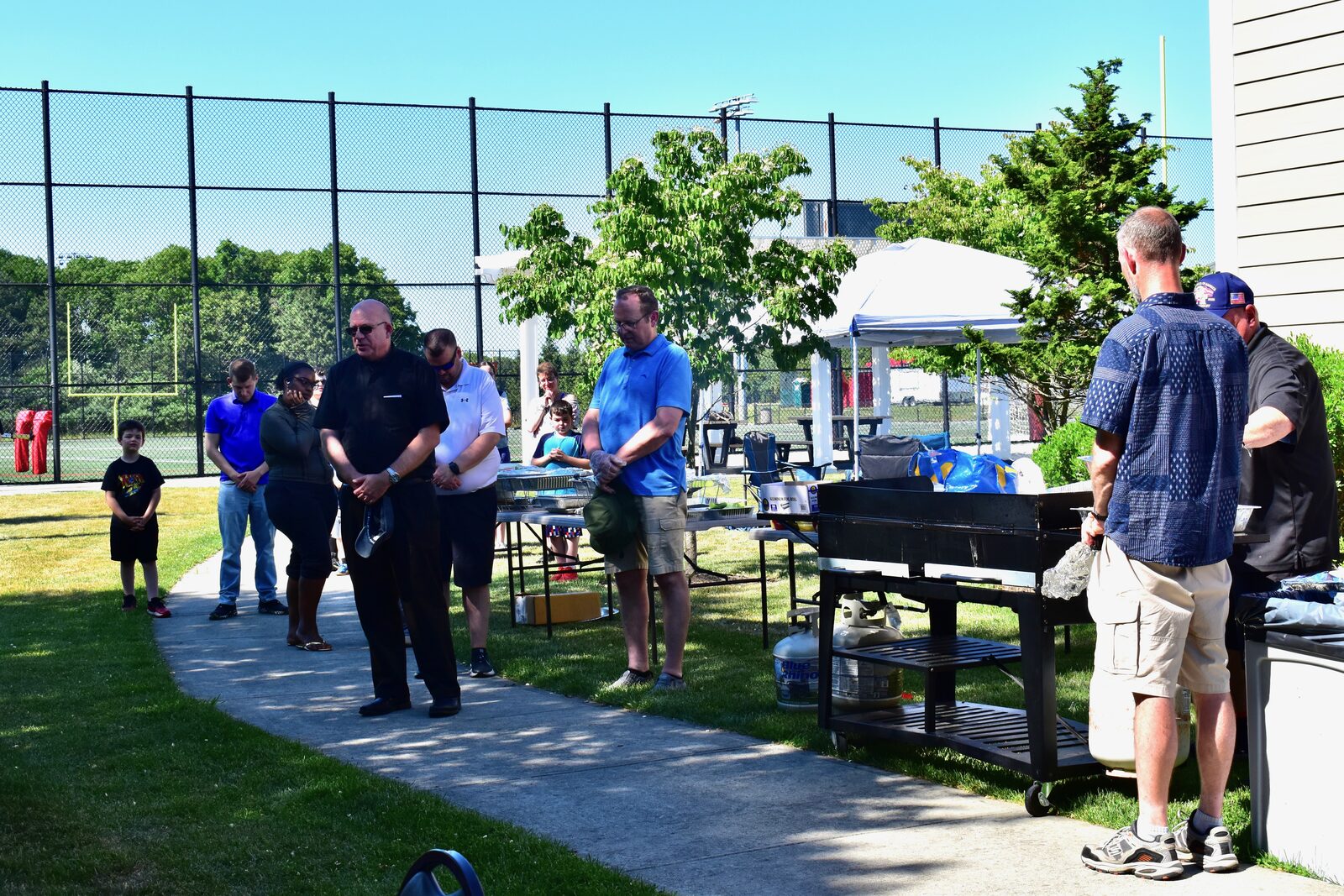 Heads bowed in prayer beside the grill at the outdoor BBQ
