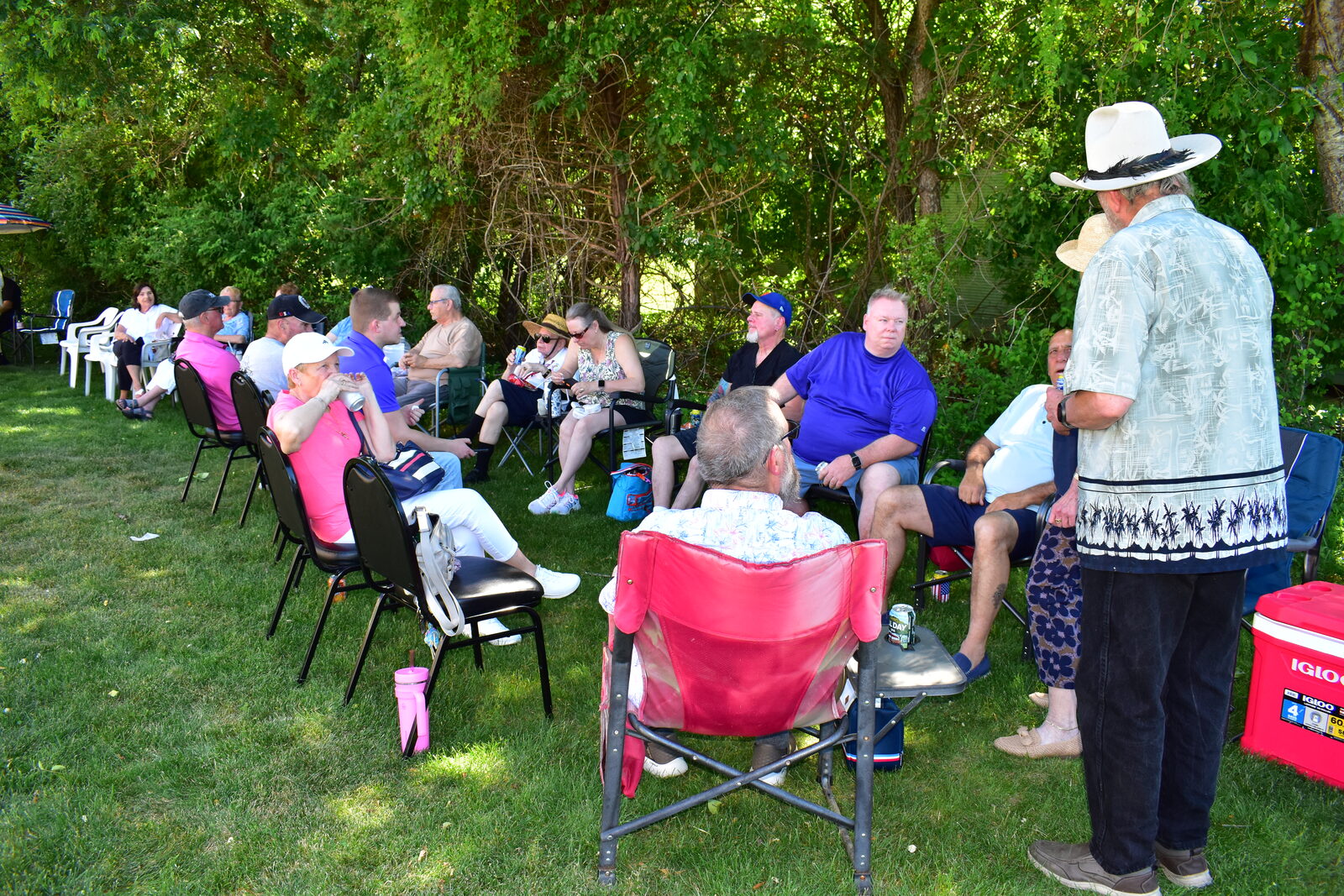 Guests seated in lawn chairs socializing in the shade at the outdoor BBQ