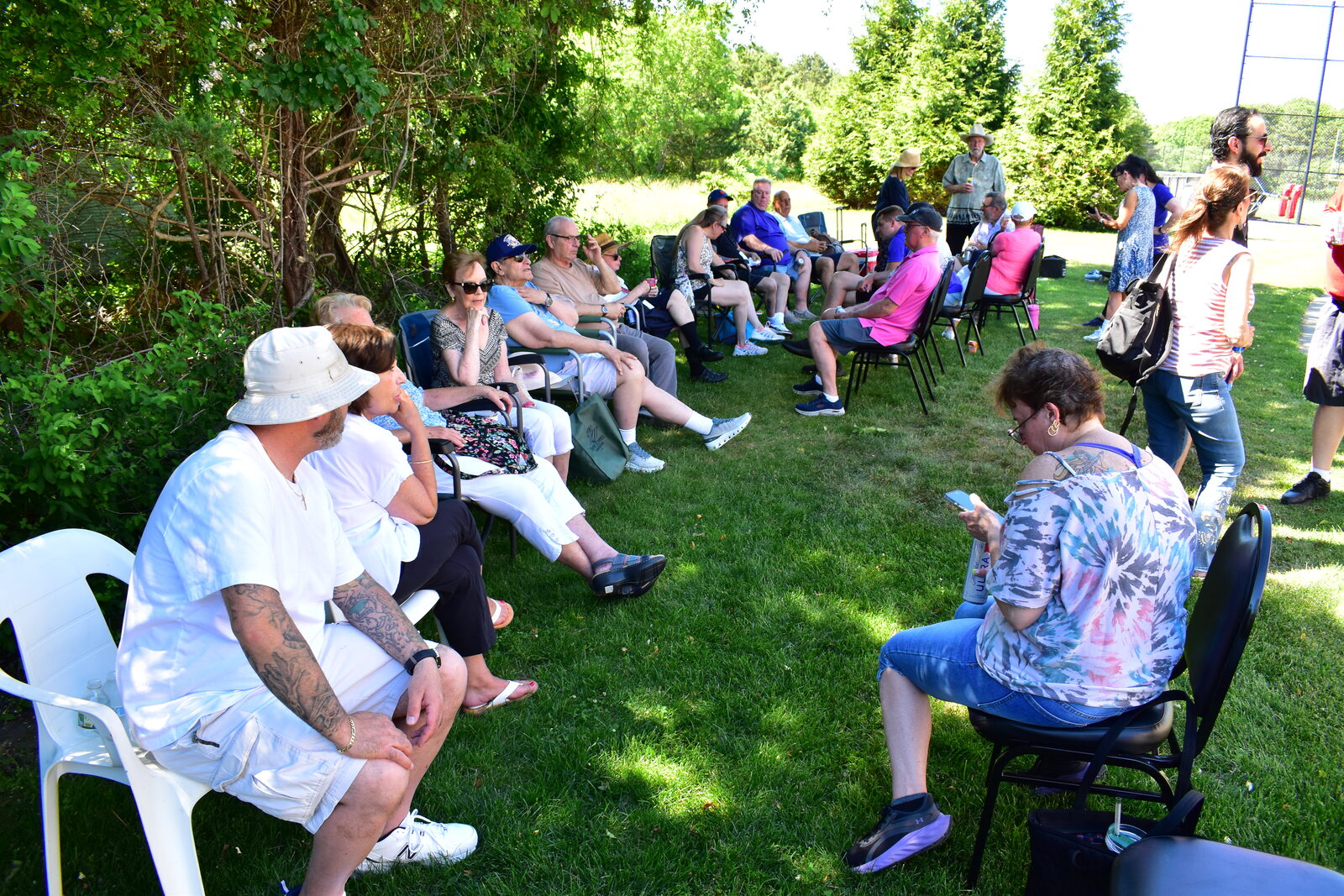 Guests gathered in lawn chairs along the shade line at the fellowship BBQ