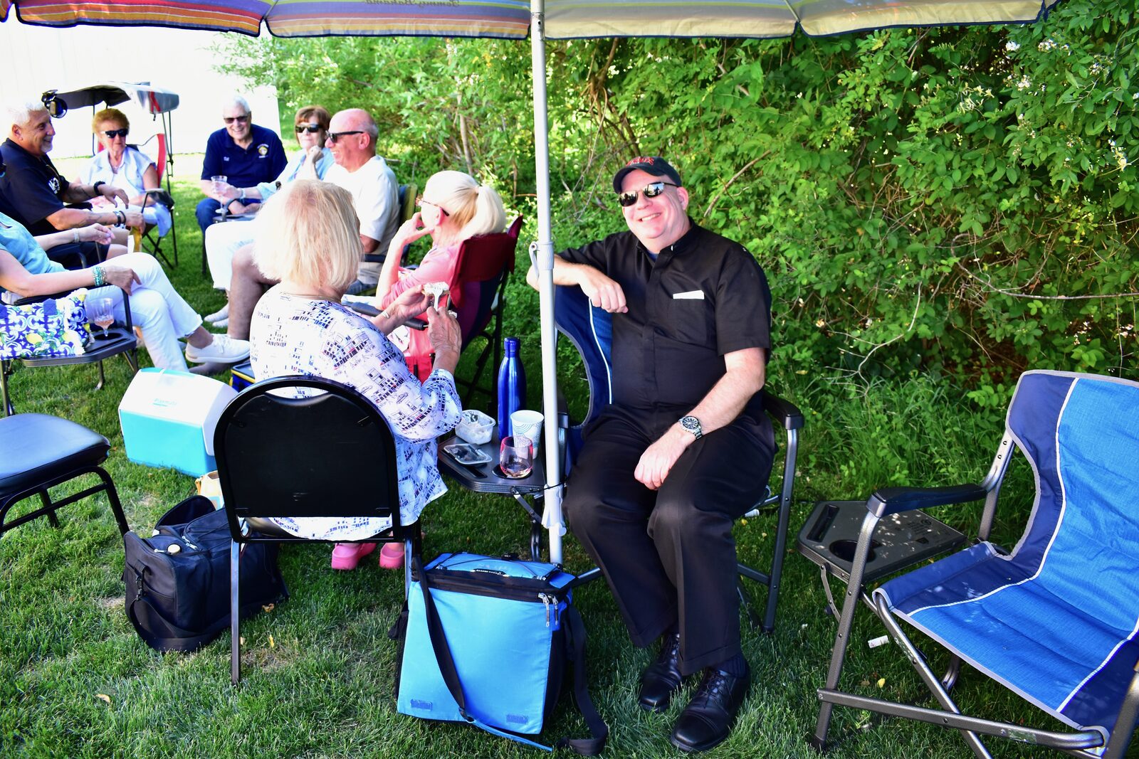 Smiling guests seated under a striped umbrella at the council BBQ