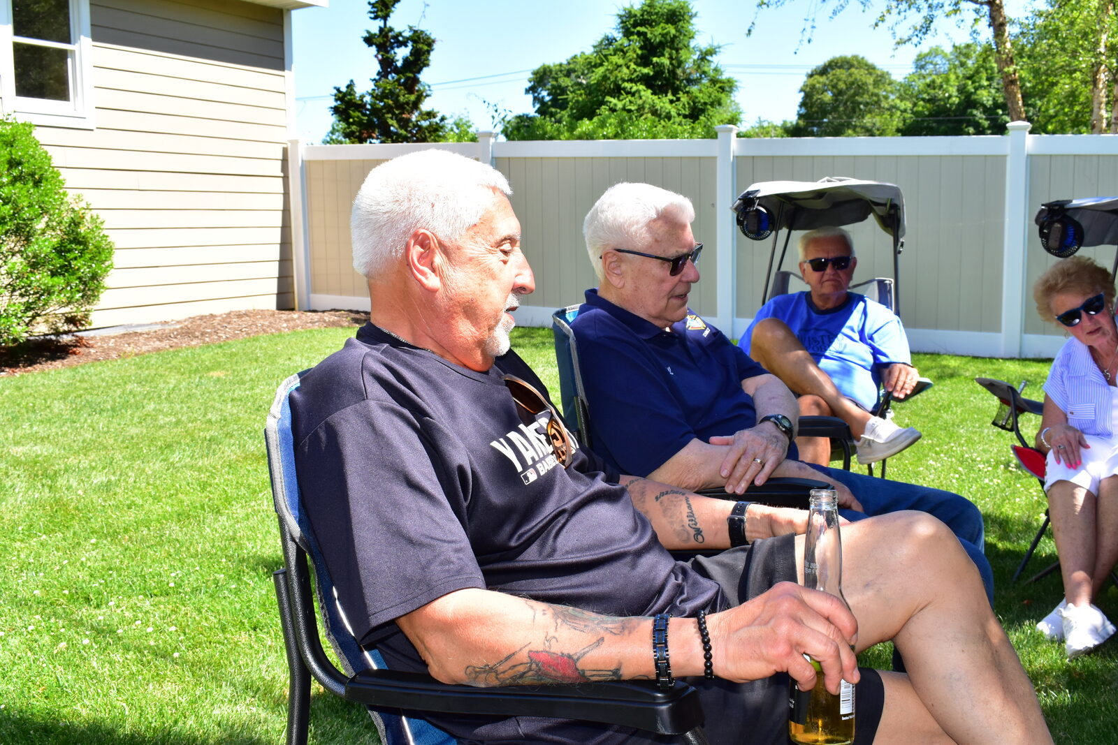 Guests relaxing in lawn chairs by the fence on a sunny BBQ afternoon