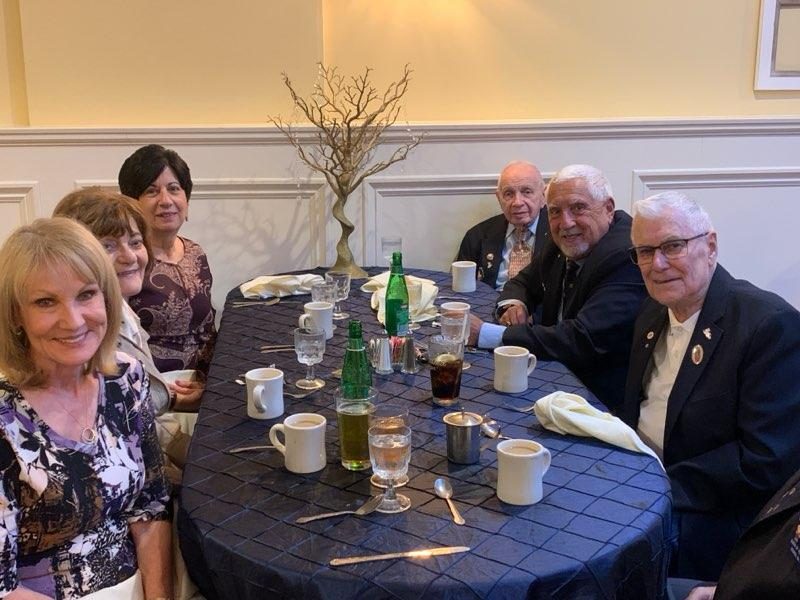 Brother Knights and family smiling together at a dinner table during the Officer Installation celebration